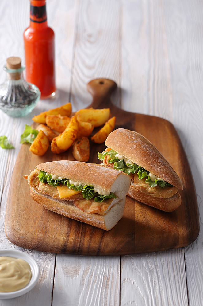Submarine sandwiches with potato wedges served on wooden cutting board.