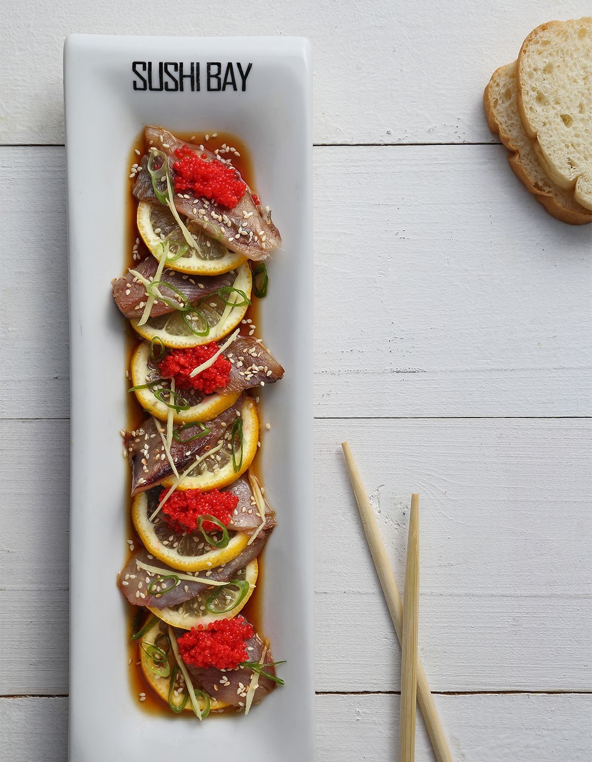 Elegant sushi platter with tuna, lemon slices and garnishes on white rectangular plate.