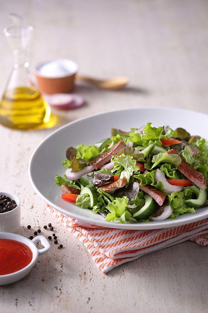 Fresh garden salad with mixed greens, tomatoes and dressing served on a white plate.