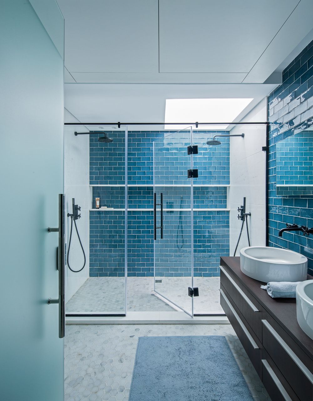 Luxurious bathroom featuring blue subway tile, glass shower enclosure, and floating vanity.