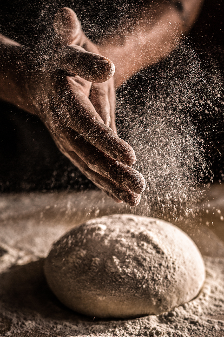 Dramatic shot of flour dusting over bread dough during the baking process.