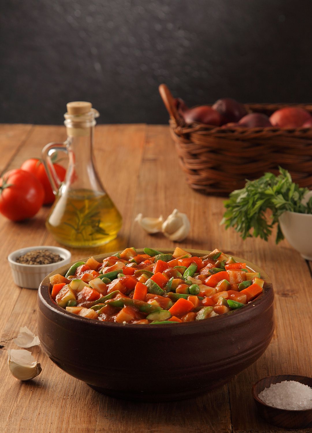 Bowl of colorful stir-fried vegetables with olive oil and spices on wooden table.