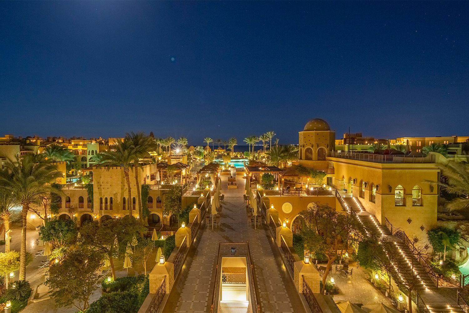Arabian resort town lit up at night with traditional architecture and palm trees.