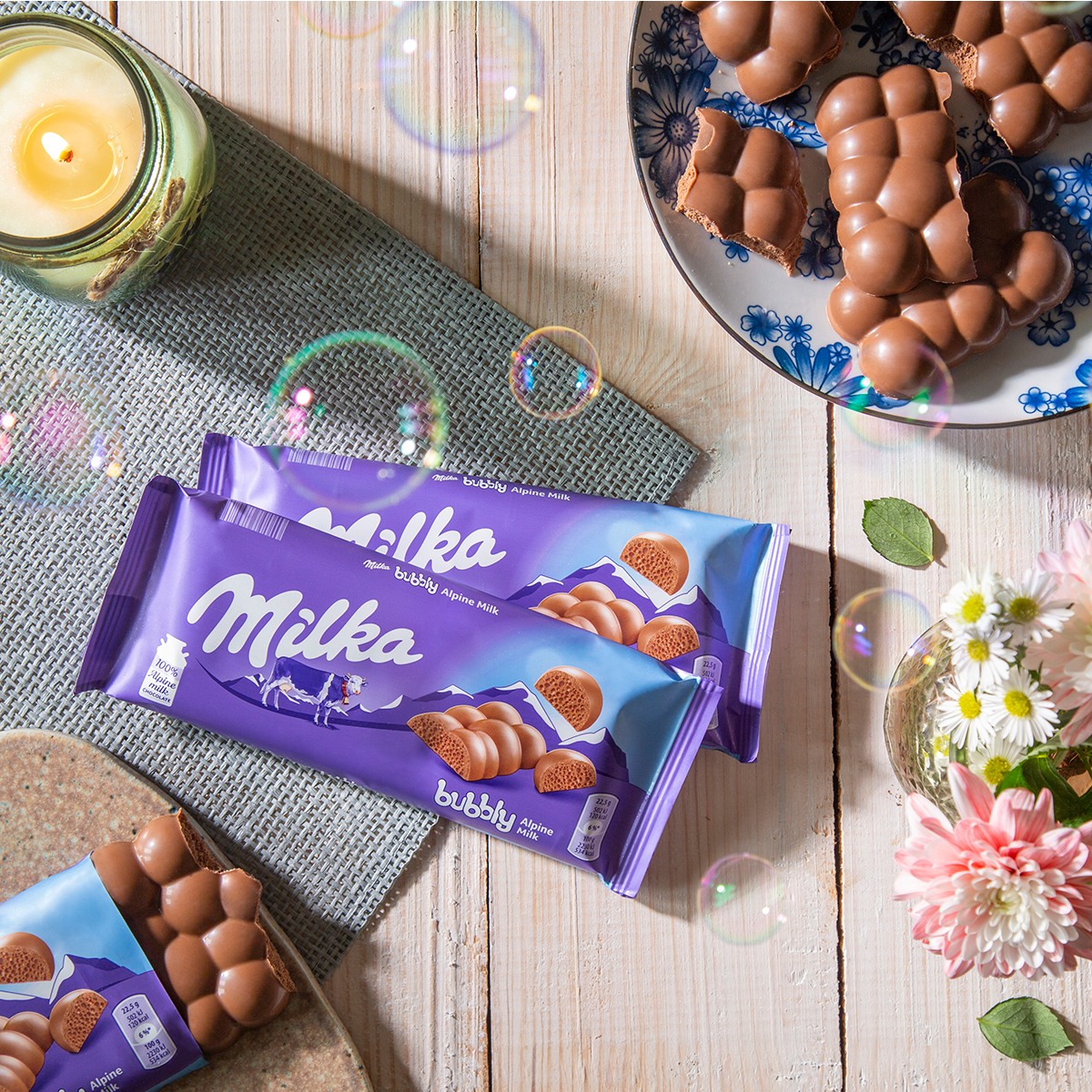 Milka chocolate bars displayed with flowers and candies on wooden table with decorative elements.