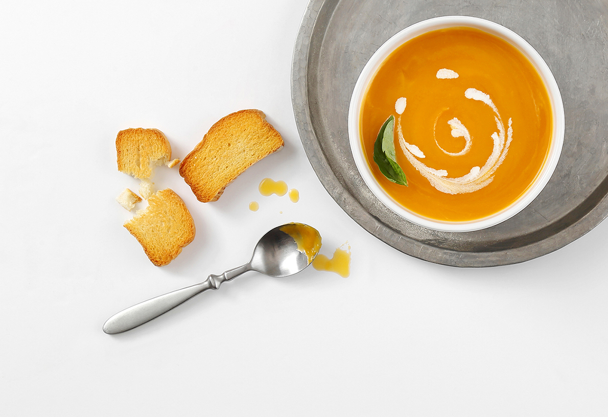Creamy pumpkin soup garnished with cream swirl and herbs served with crispy bread.