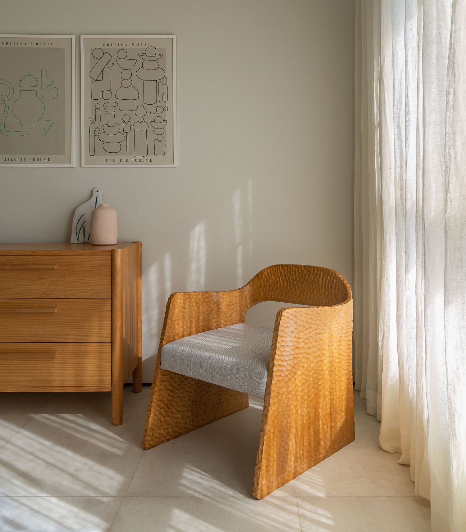 Stylish curved wooden armchair with gray cushion next to a dresser in a sunlit corner.