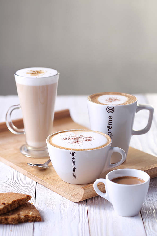 Assorted coffee drinks in white cups arranged on wooden serving board with latte art.