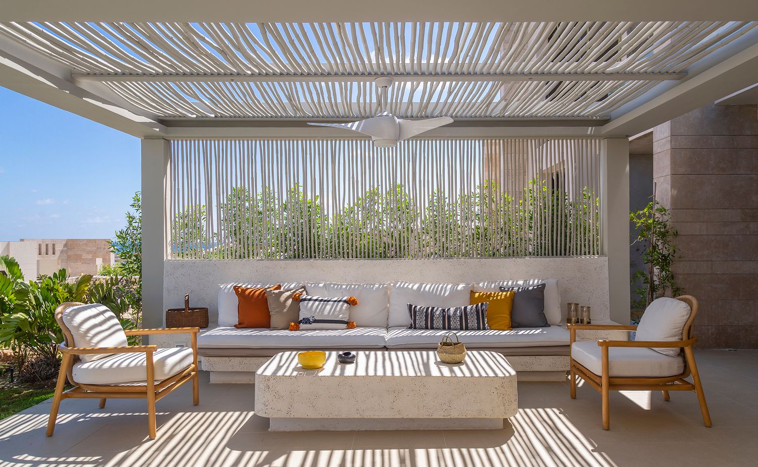 Outdoor living space with wooden pergola and comfortable seating featuring orange accent pillows.