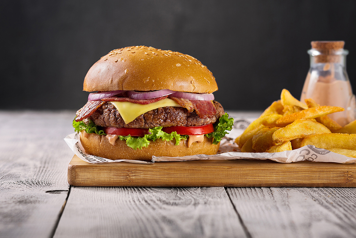 Juicy cheeseburger with lettuce and tomato served with french fries on wooden board.