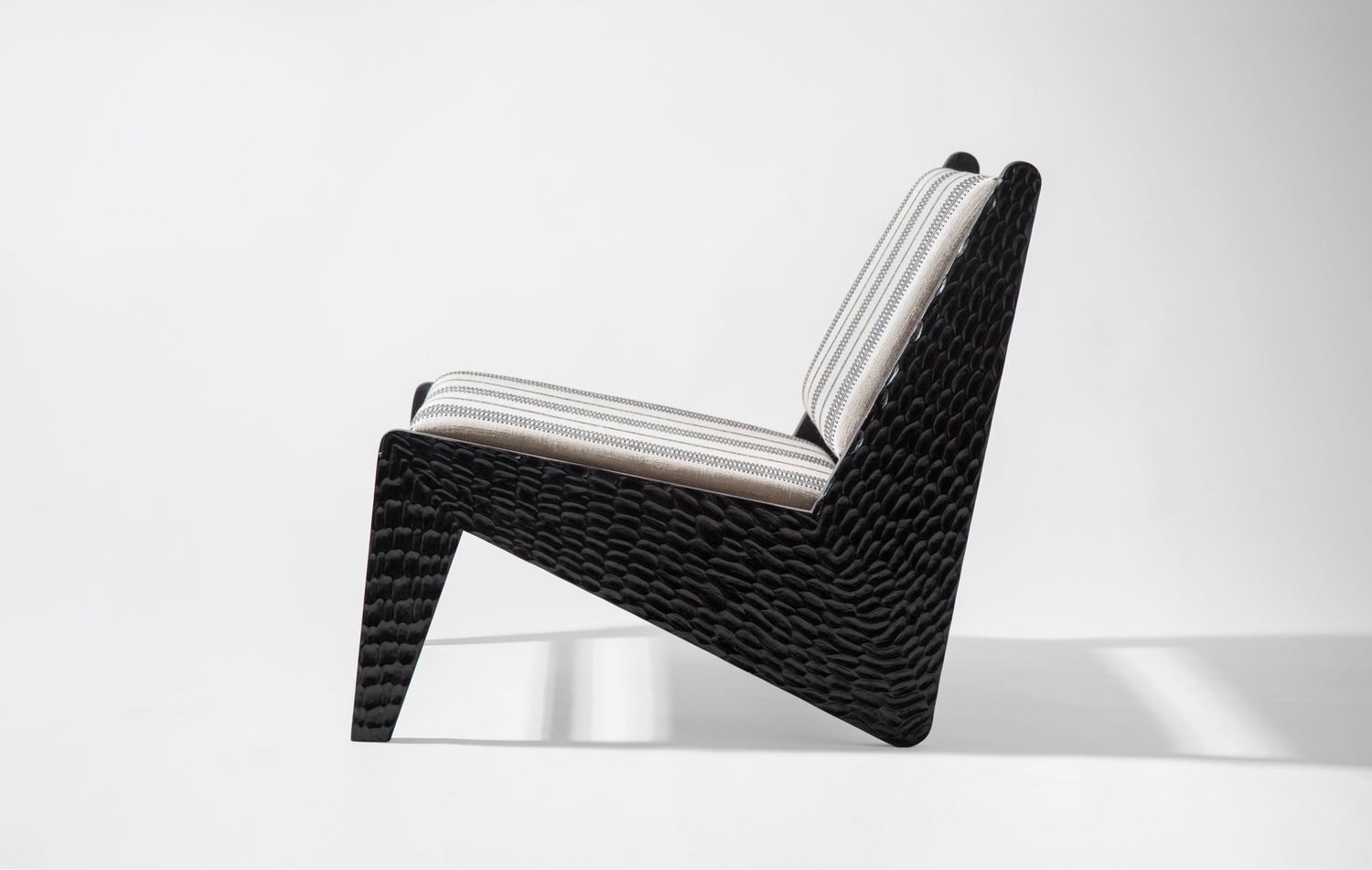 Minimalist black lounge chair with white cushioning against white background.