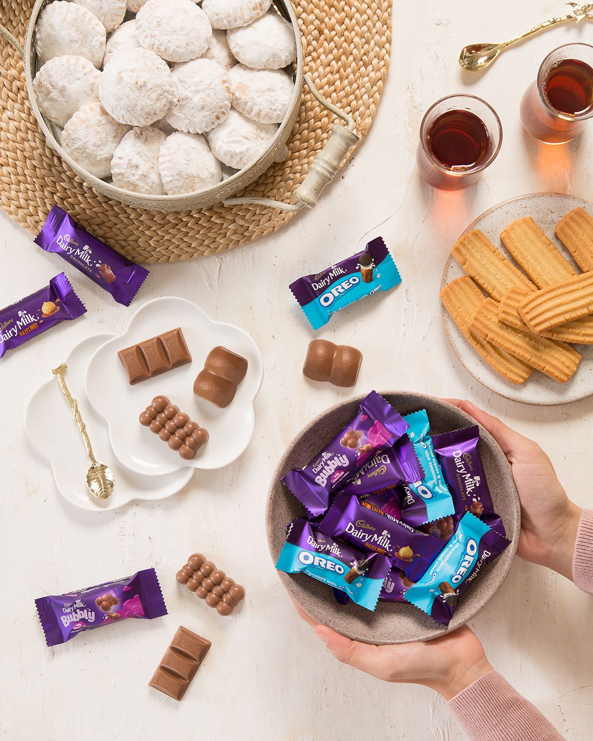 Flatlay of Cadbury chocolates, powdered cookies, and tea served with biscuits on a textured surface.