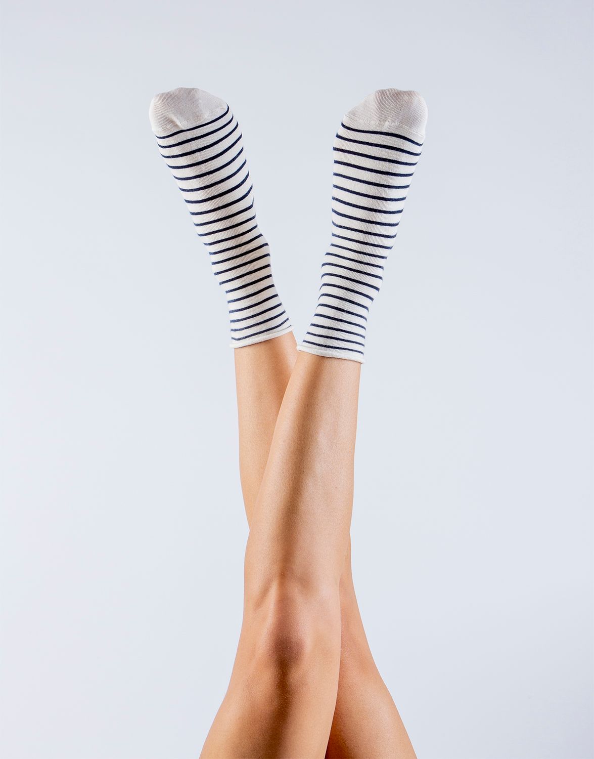 Legs wearing black and white striped socks crossed and raised against a light gray background.