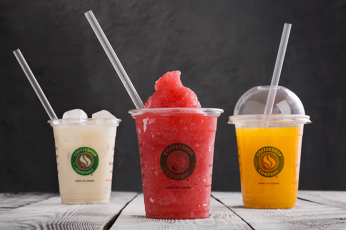 Three colorful frozen slushies in clear cups with straws against dark background.