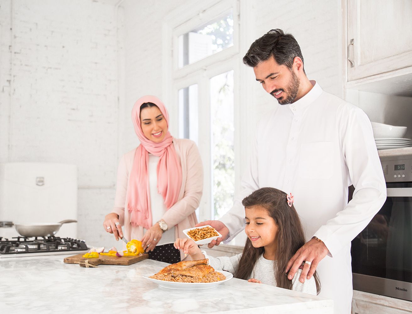 Family preparing food together in a bright modern kitchen with white countertops.