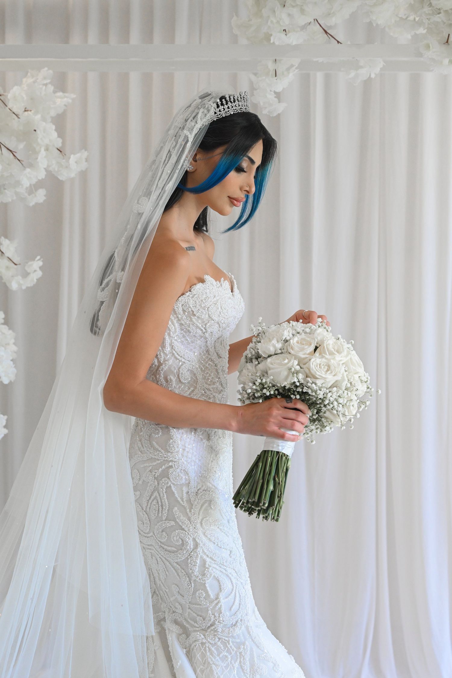 A bridal portrait featuring an intricately detailed lace gown and white bouquet.