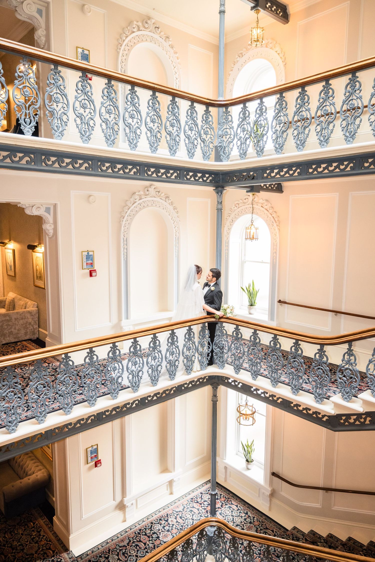 Elegant Victorian staircase with ornate iron railings and white walls illuminated by natural light through arched windows.