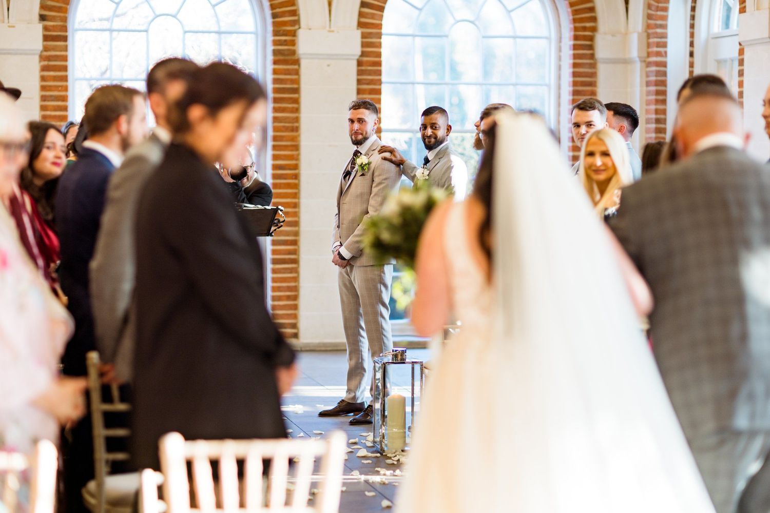 A wedding reception venue filled with guests mingling in an elegant space with brick archways and natural light.