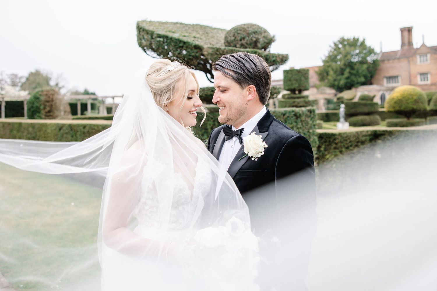 An elegant couple shares a romantic moment on a rustic bridge overlooking a tranquil pond on their special day.