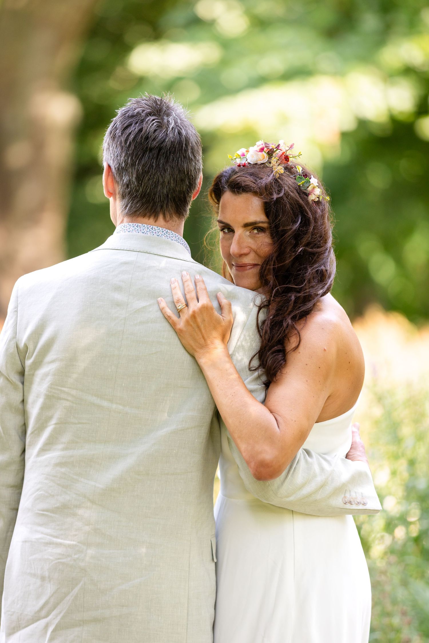 A couple shares an intimate moment outdoors on their wedding day, with soft natural lighting and greenery in the background.