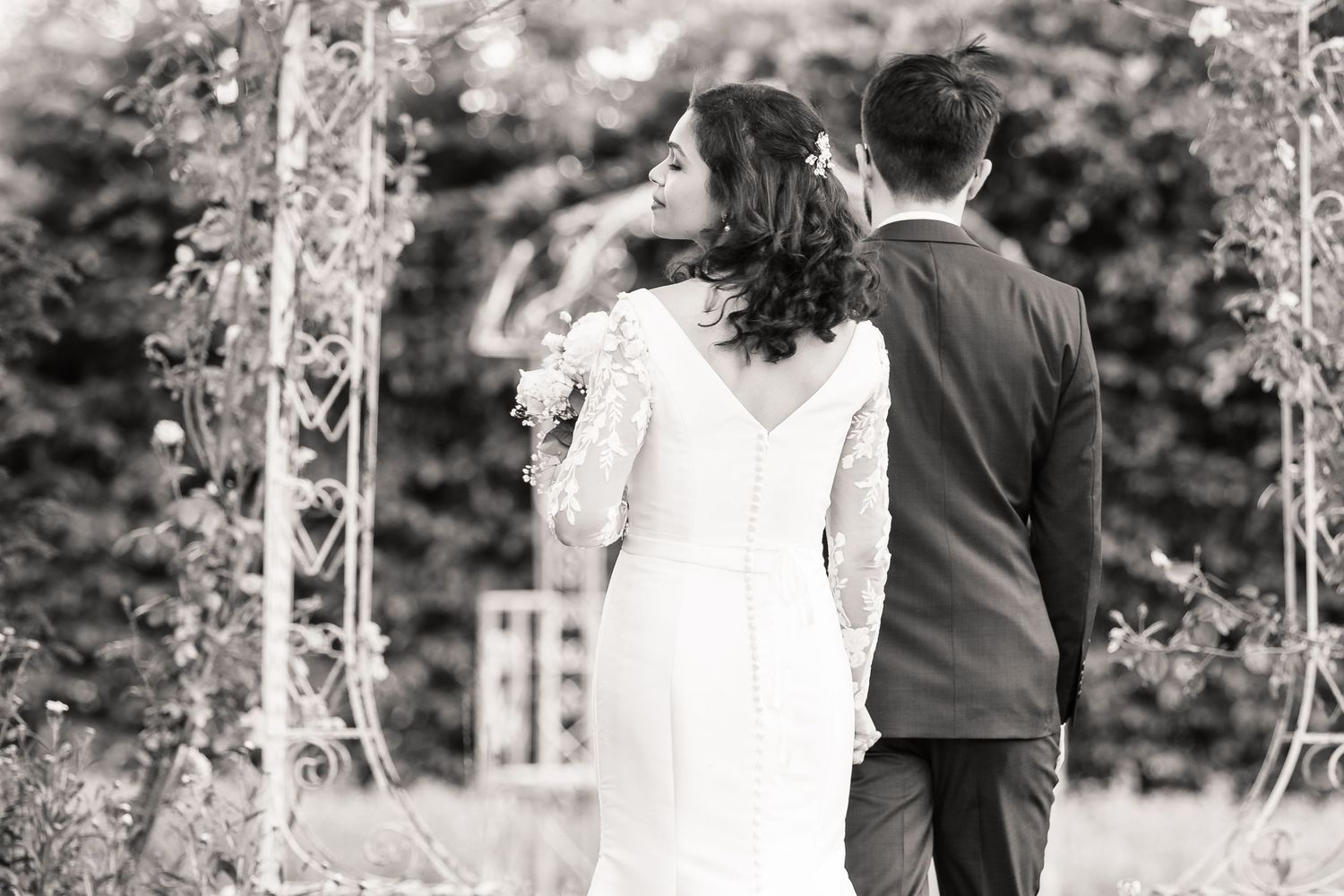 A black and white image of a couple under an archway during their wedding ceremony, captured from behind.