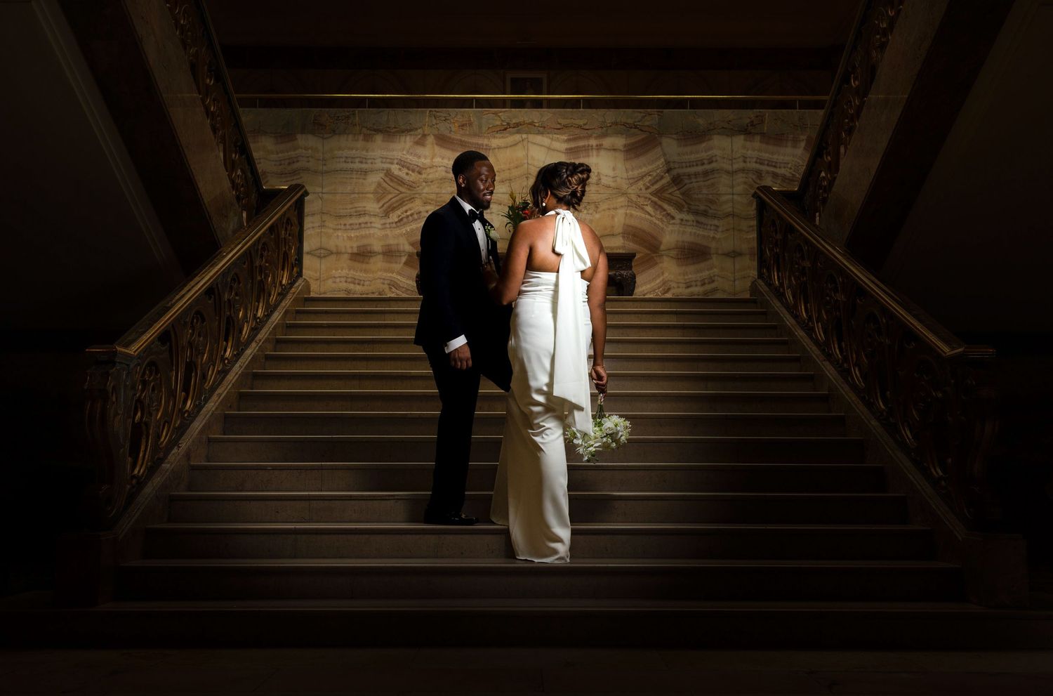 Shelana and Peter’s wide couple portrait sharing a look on the stairs at their London wedding, captured by Oisin Studios