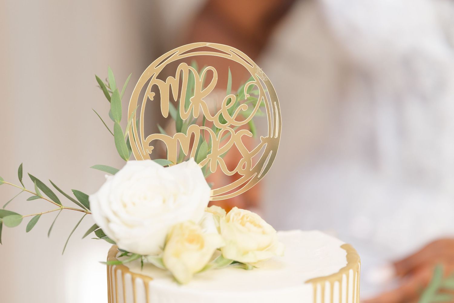 Elegant wedding cake with blush pink frosting and fresh white roses adorned with a decorative gold cake topper.