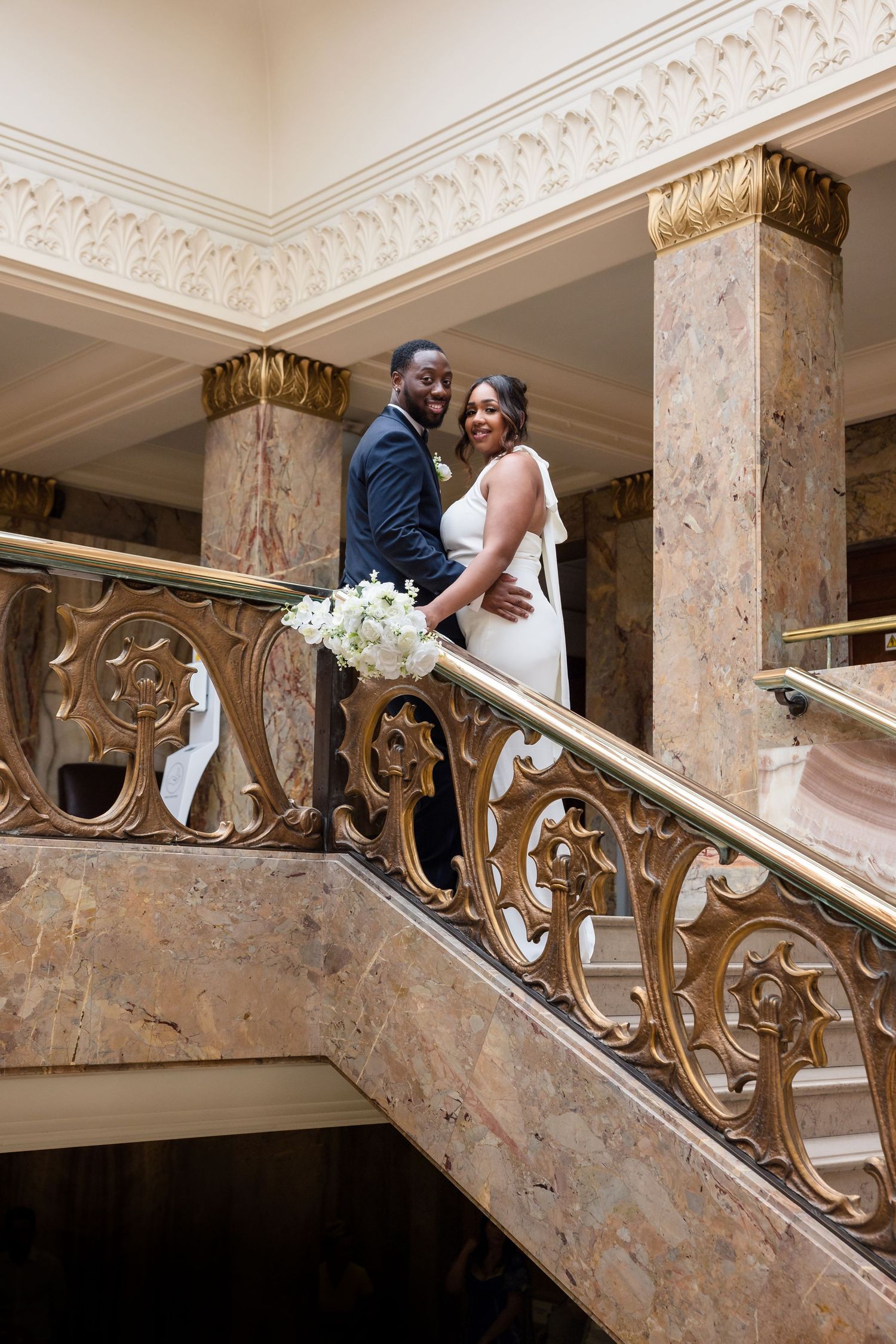A romantic couple shares an intimate moment on an ornate marble staircase with decorative gold railings.