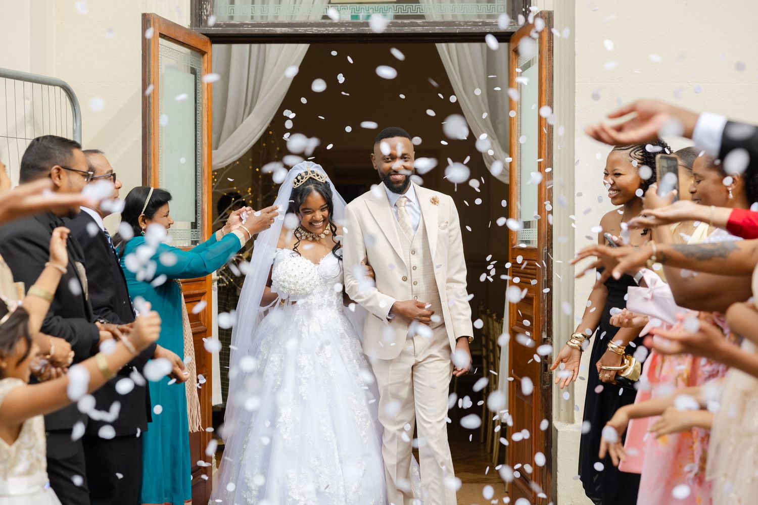 Wedding guests toss rose petals in celebration as couple exits down a row of well-wishers at their ceremony.
