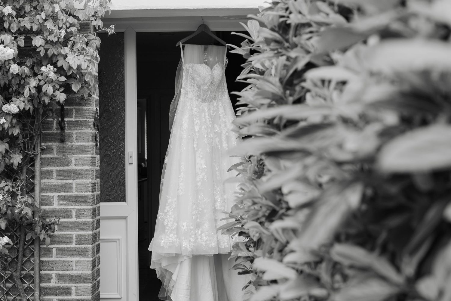 Black and white wedding dress photo displayed among leaves and brick walls against dark backgrounds.