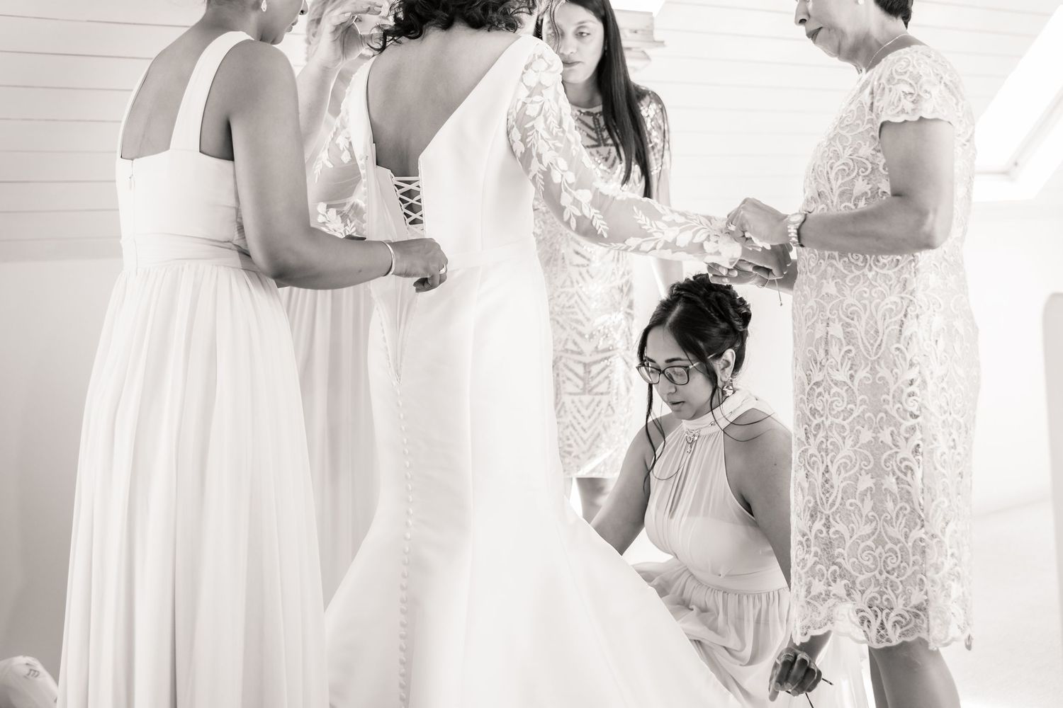 Emotional moment captured in black and white as bridesmaids help with wedding dress preparations.