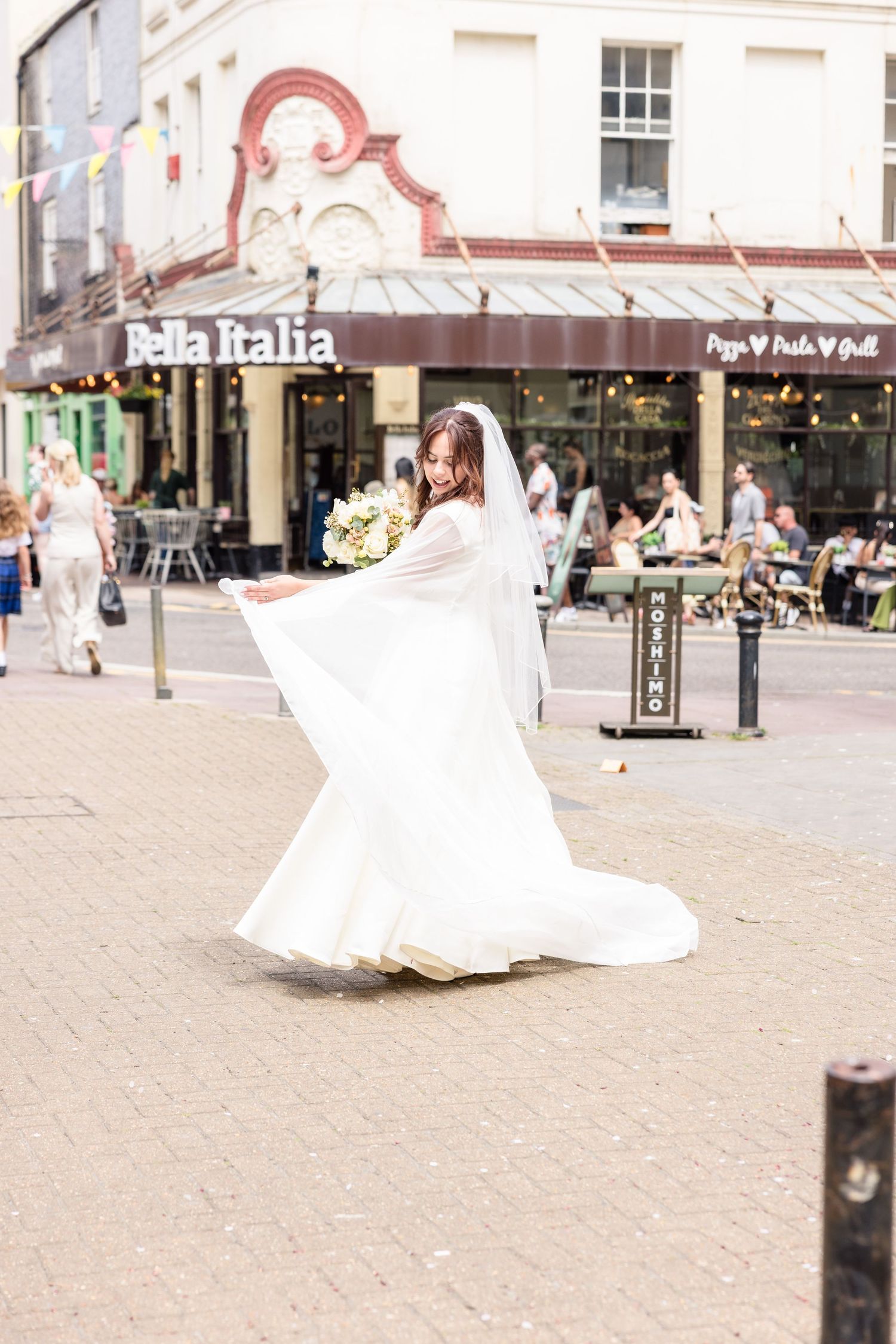 A series of four connected images showing someone in a flowing white wedding dress twirling on a city square.