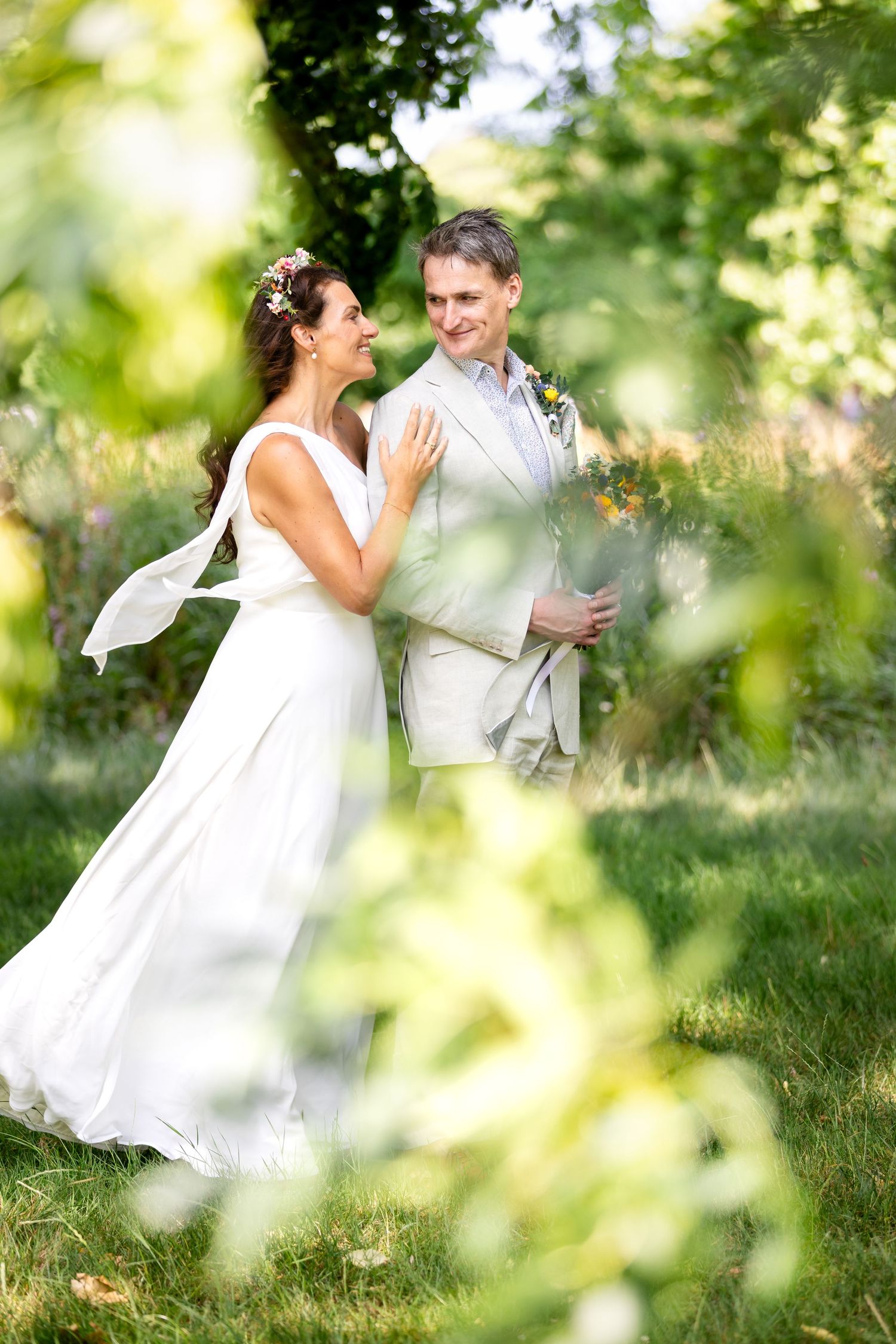A couple in wedding attire shares an intimate moment in a sun-dappled garden setting with soft bokeh effects.
