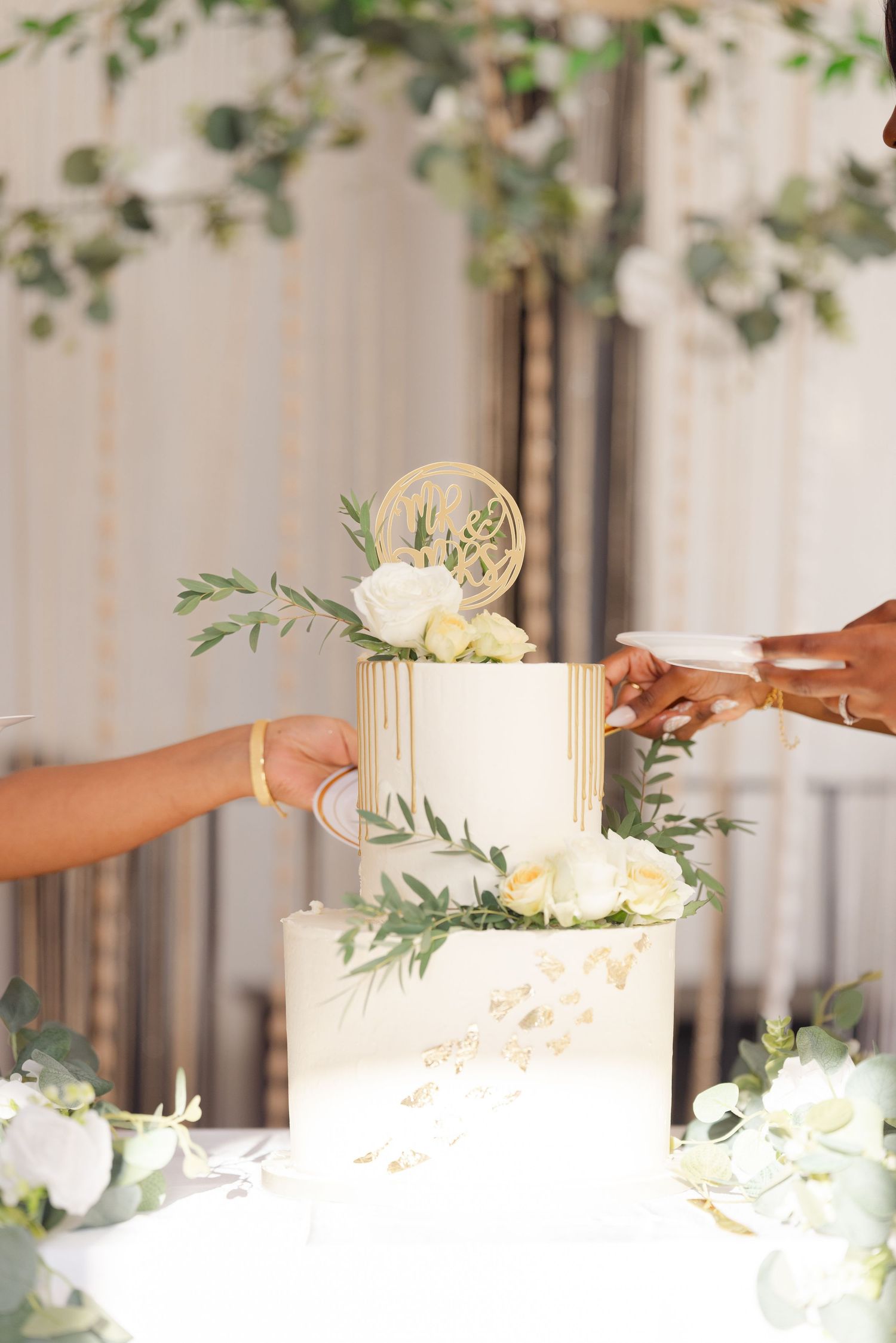 Three white pillar candles arranged on a table with greenery and floral decorations for an elegant event.