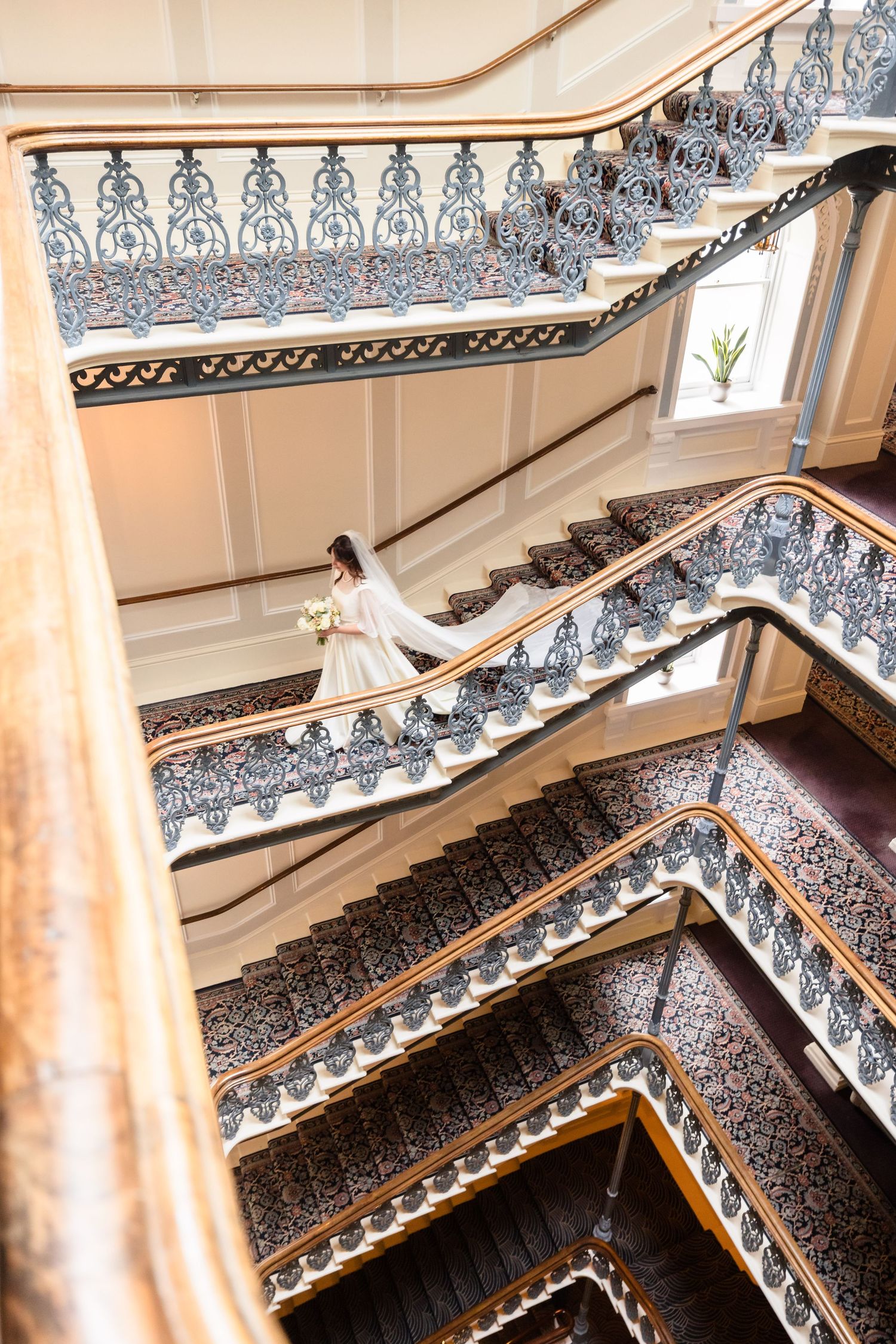 Ornate Victorian staircase with intricate wrought iron railings and white walls in a grand historic building interior.