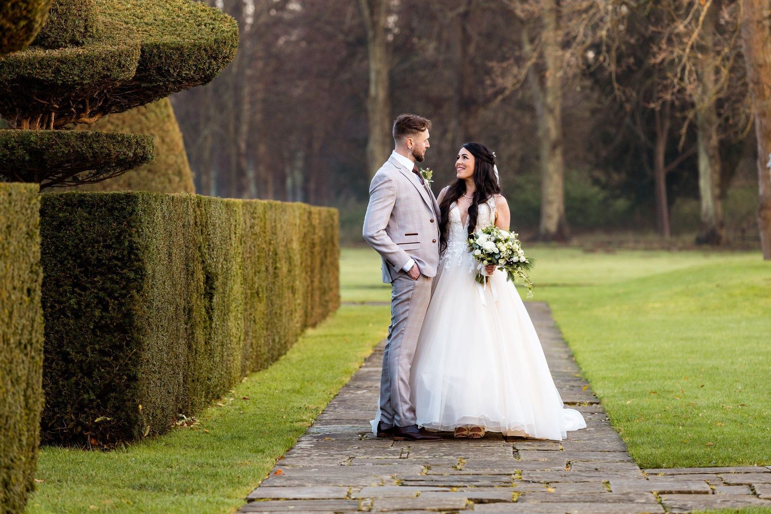 Couple shares romantic wedding moment on stone path beside moss-covered garden wall.