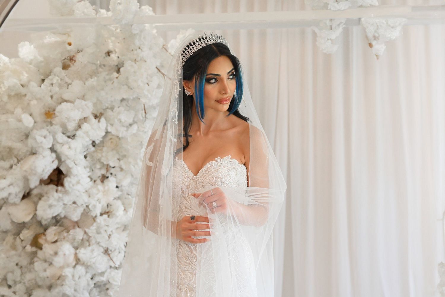 Close-up bridal portrait with delicate veil and white floral backdrop.