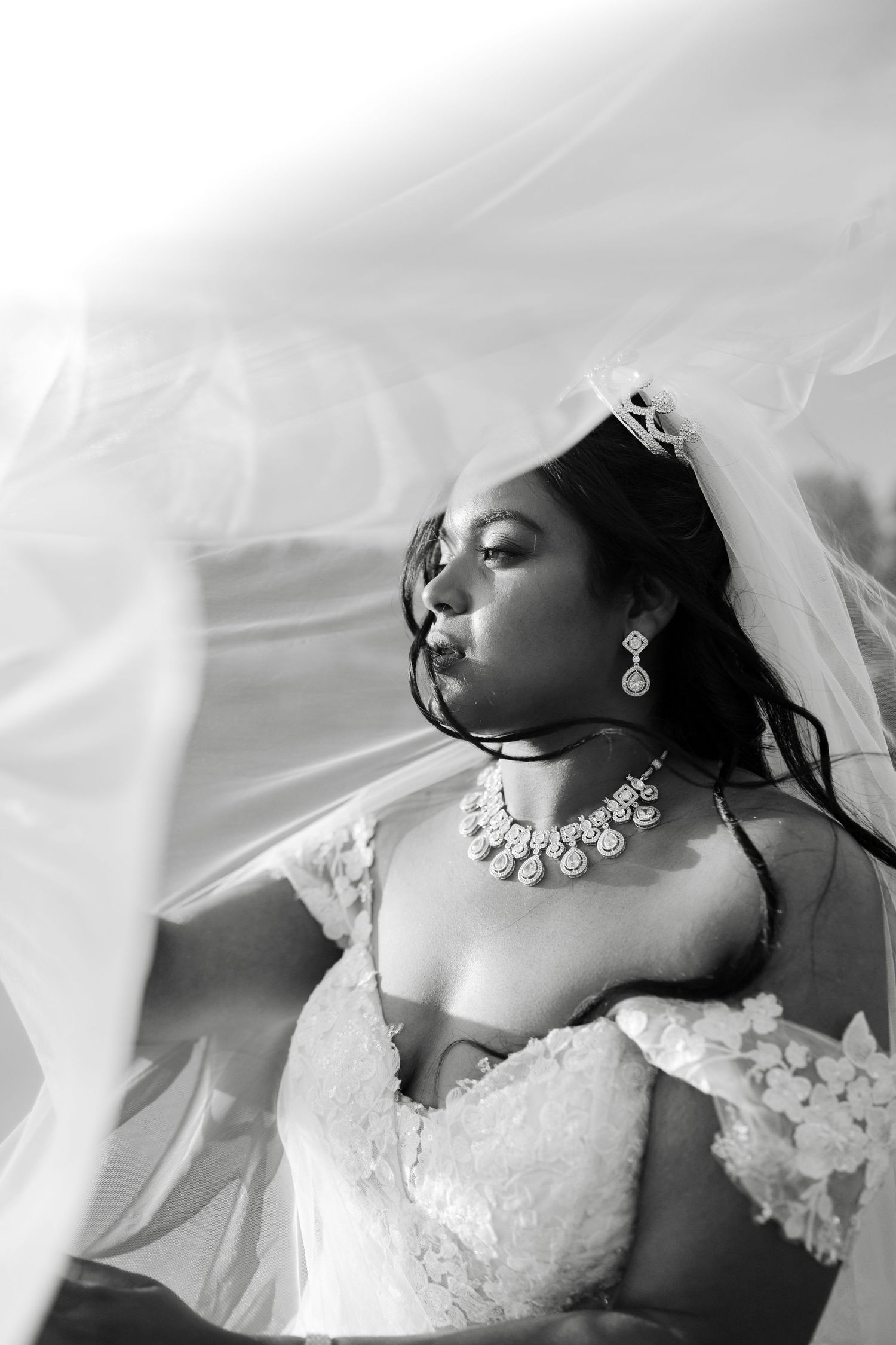 A bride in a white lace wedding dress and veil poses gracefully while laying down for an artistic portrait.