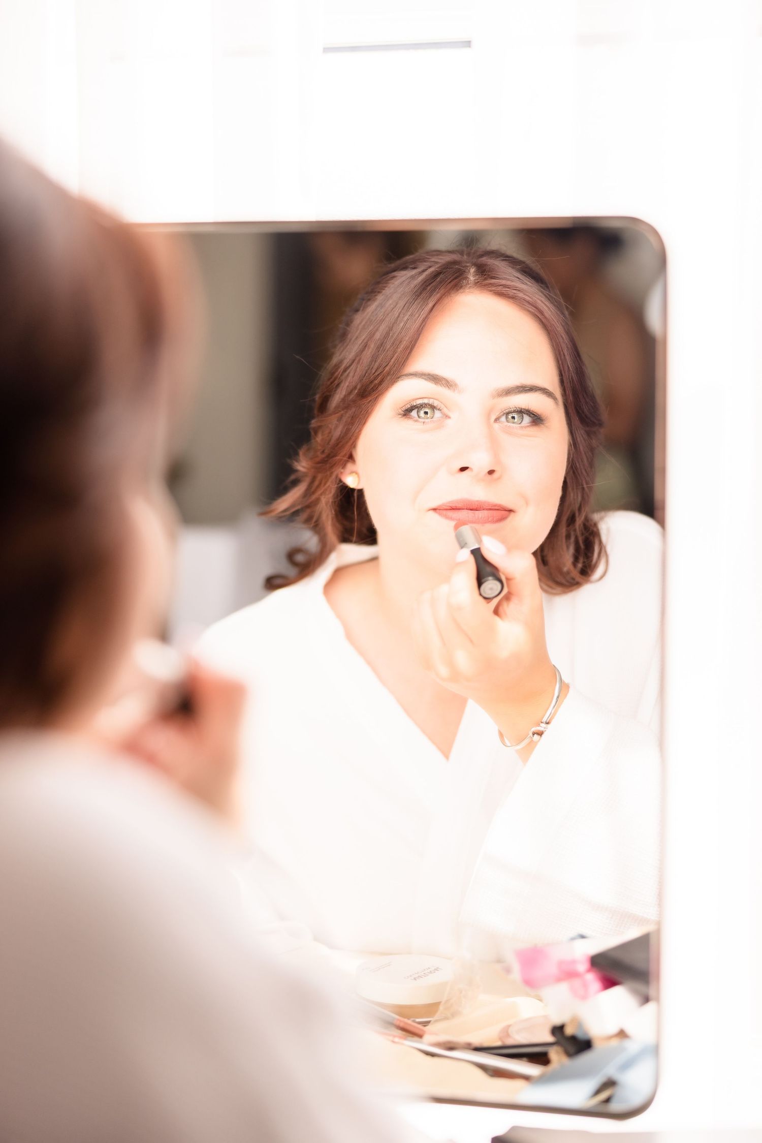 A reflection in a makeup mirror shows a woman in white getting ready for her special day.