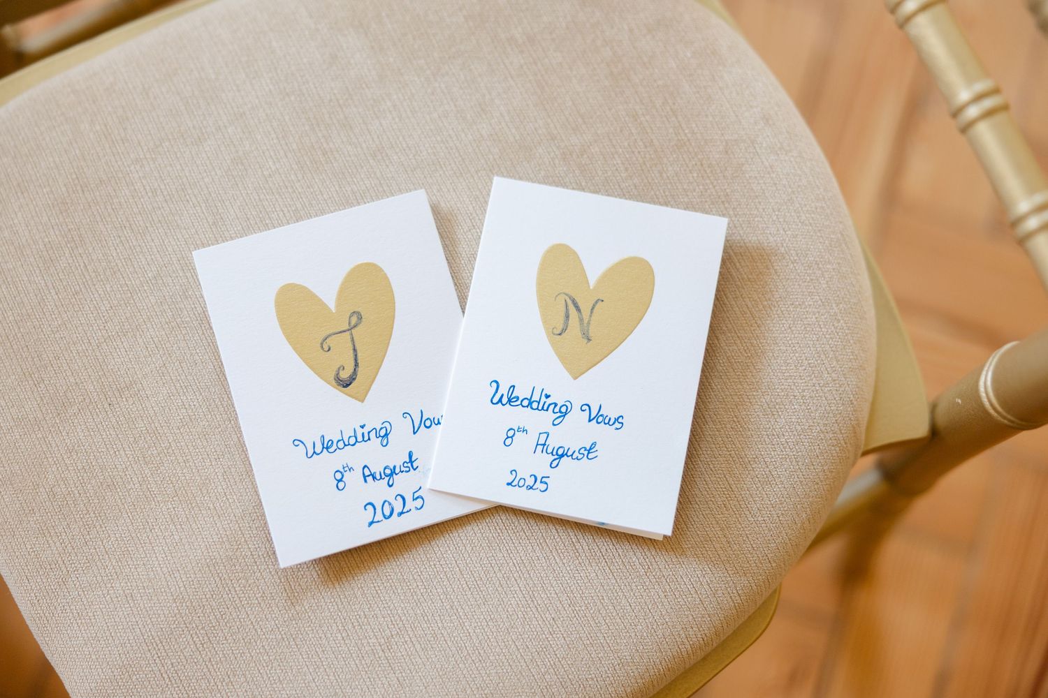 Two white wedding vow notebooks with gold hearts on the covers rest on a beige surface.