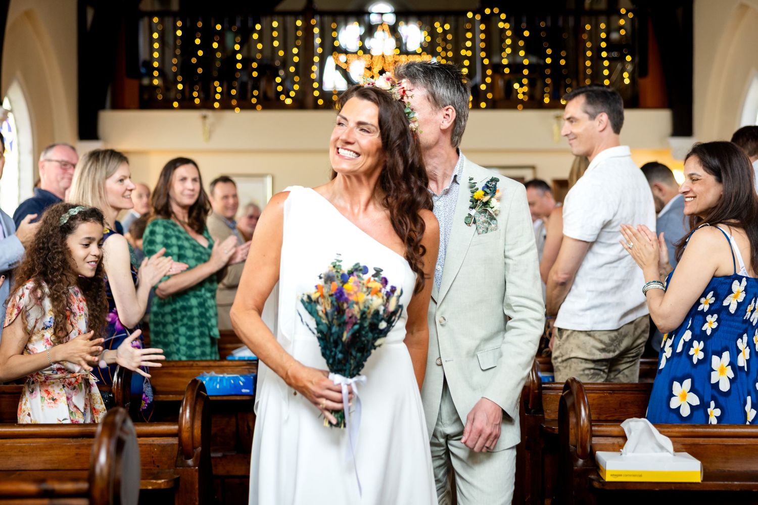 Candid sequence of wedding party guests celebrating, dancing, and embracing at a festive reception with string lights.