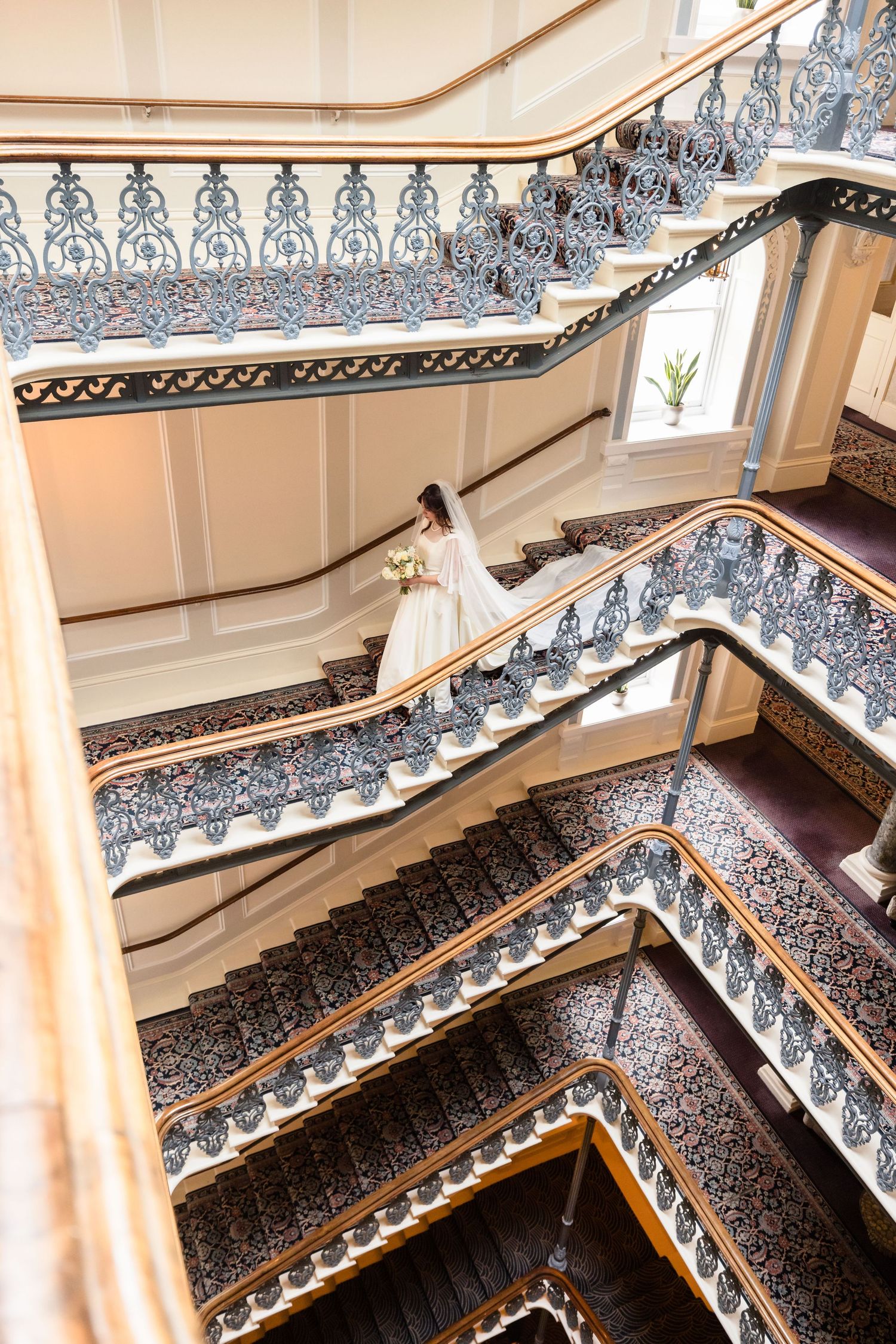 Ornate Victorian staircase with intricate black and white wrought iron railings and a flowing white dress visible on the steps.