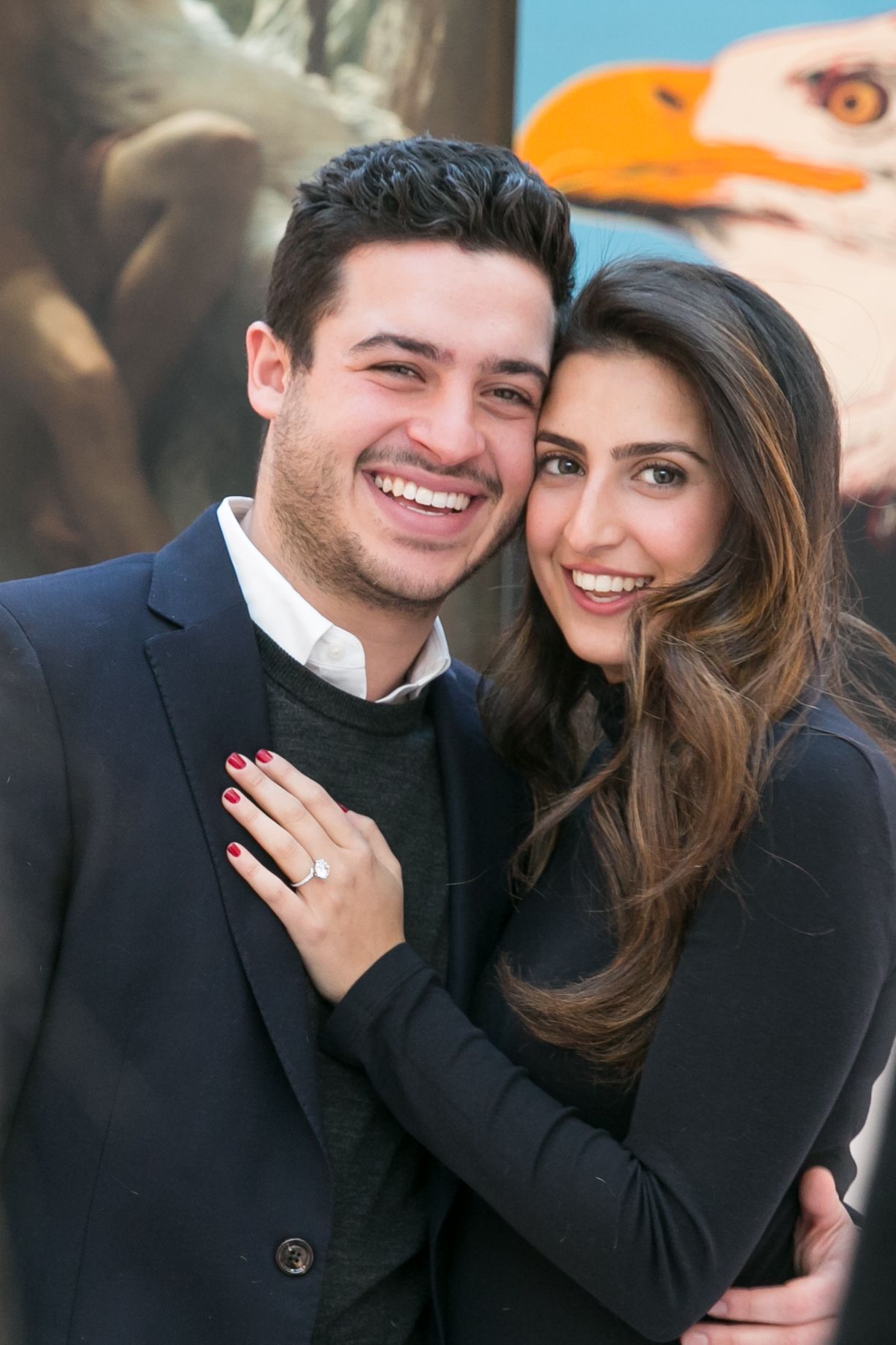 Happy couple embracing and smiling, woman showing off engagement ring.