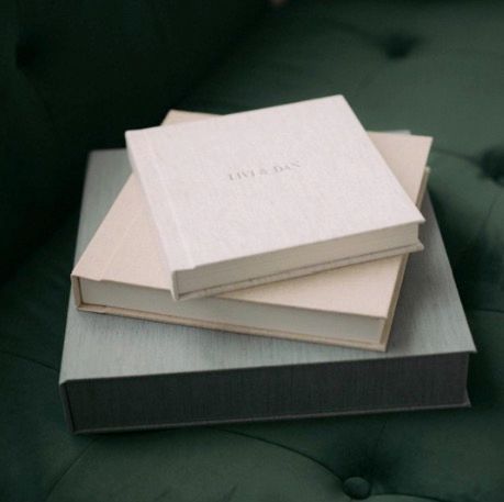 Two elegant linen-covered photo albums stacked on a green velvet chair.
