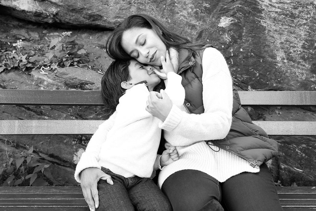 Black and white photo of a mother and child sharing a tender embrace on a bench outdoors.