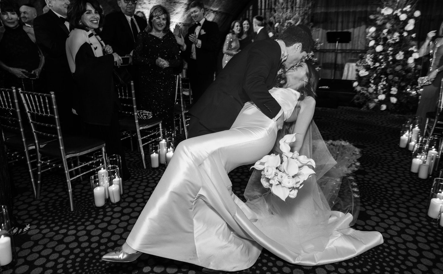 Black and white photo of groom dipping bride for a kiss at the end of their wedding ceremony.