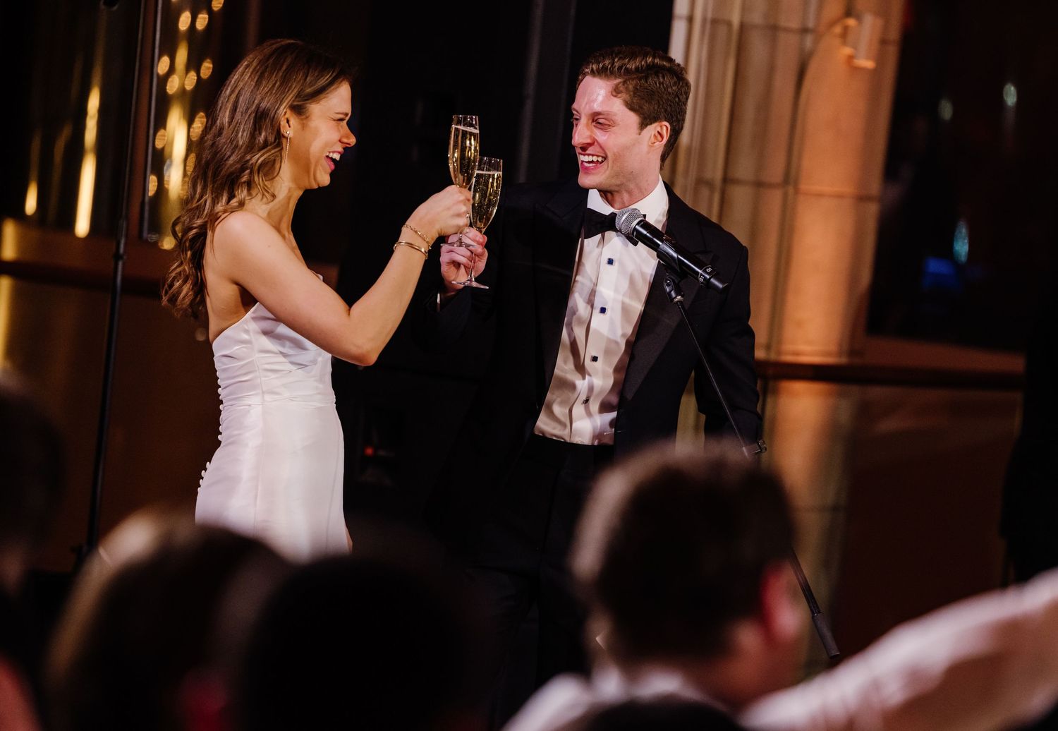 Bride and groom laughing while toasting champagne glasses at wedding reception.