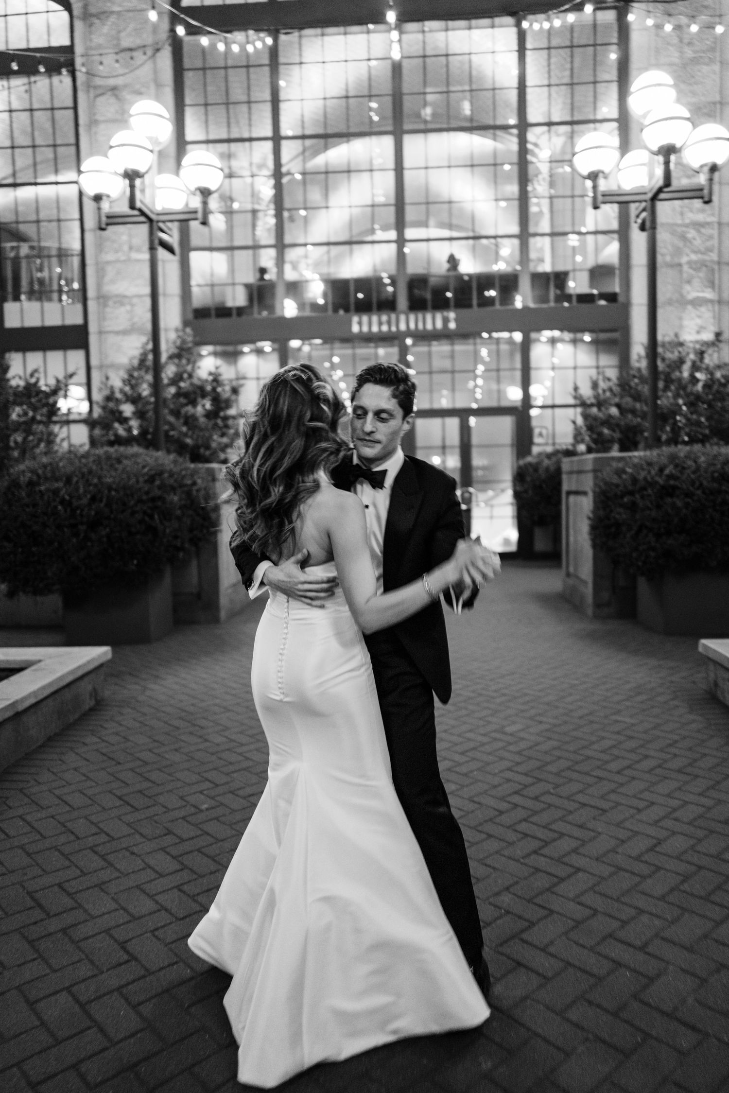 Bride and groom share a romantic first dance outside an elegant venue at night in black and white.
