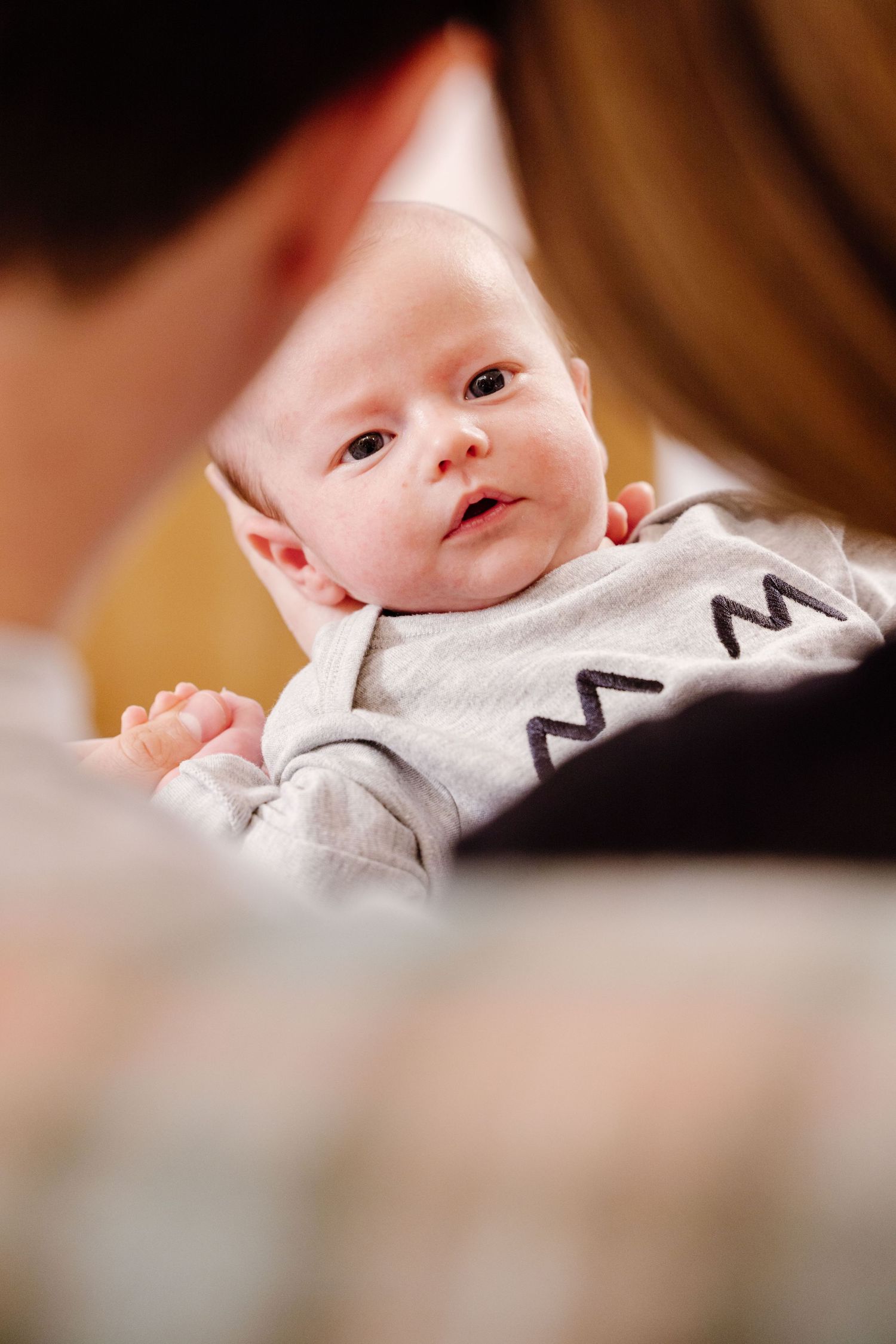 Newborn baby in a grey onesie being held and gazed at lovingly by both parents.