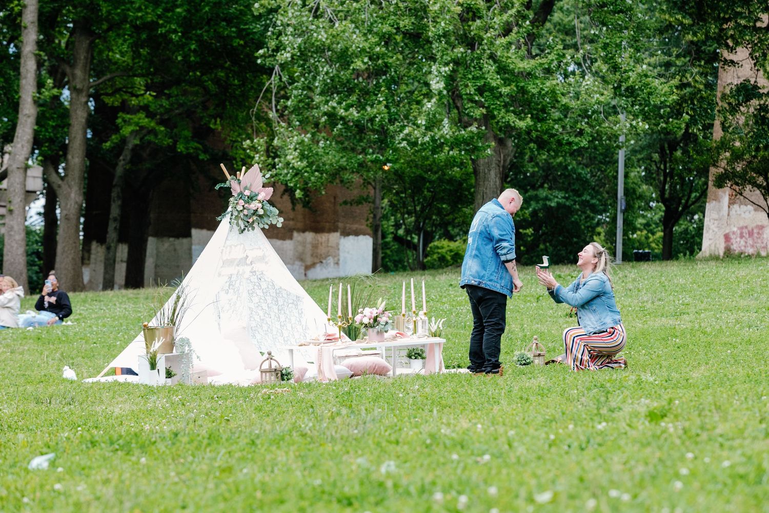 Outdoor marriage proposal in park with decorative teepee and floral arrangement.