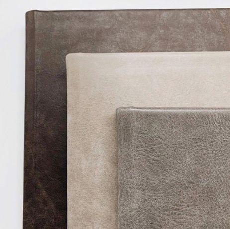 Three stacked leather-bound journals in dark brown, cream, and gray tones showcasing premium textured covers.